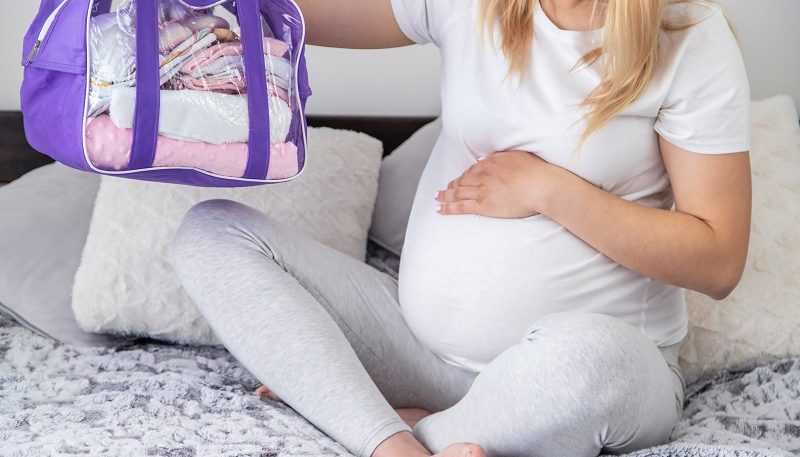 Fotografía de mujer embarazada preparando maleta para el bebé