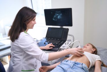 Female conducts an ultrasound of the internal organs of a little girl, the doctor communicates kindly with a young patient