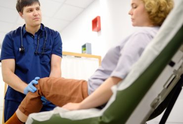 Woman at an appointment with rheumatologist talks about pain symptom of knee joint. Orthopedic doctor examines a patient. Rheumatology deals with circulatory, lymphatic systems and autoimmune diseases